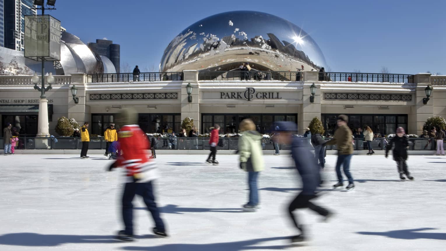 Blurry ice skaters zoom past, the reflective Bean is visible in the distance