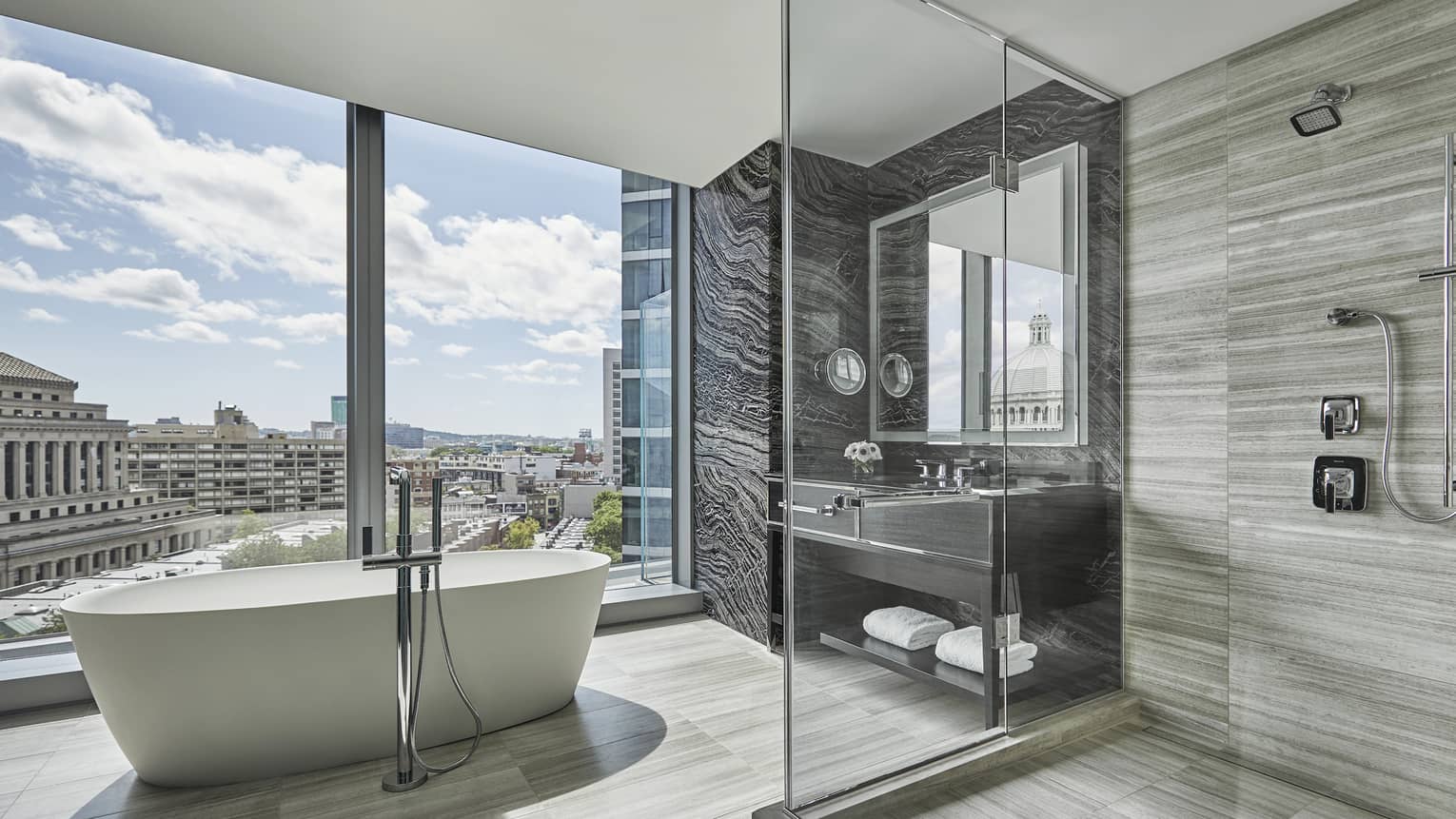 A free-standing tub sits in the middle of a large neutral bathroom, surrounded by floor to ceiling windows, at four seasons hotel boston one dalton
