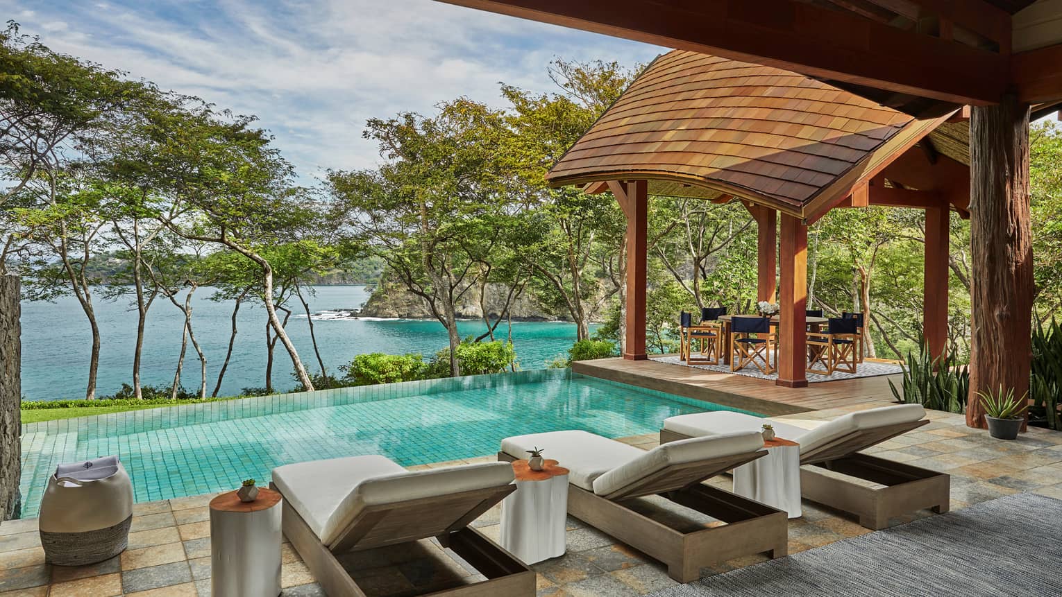 Miramar Suite patio tile patio, three long lounge chairs in front of plunge pool, row of trees, overlooking ocean