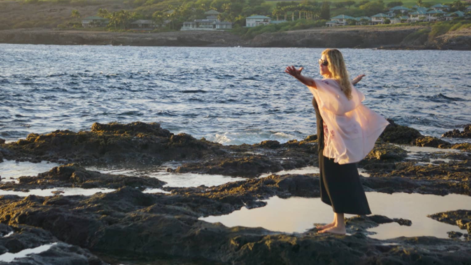 A woman meditates at edge of ocean on lava rock