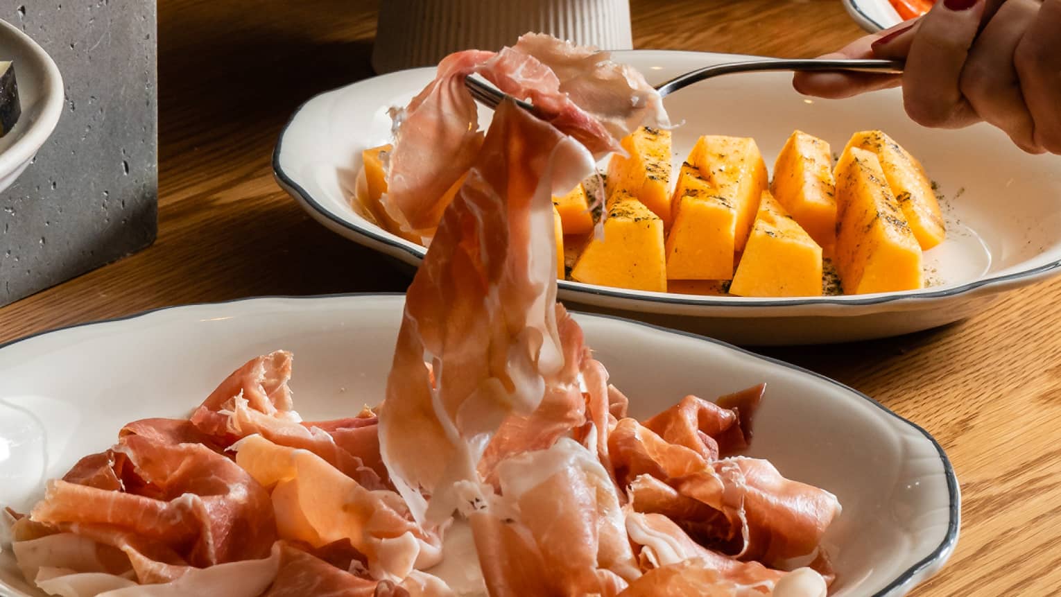An aperitivo table laden with beautifully plated meats, olives and salads, a fork lifting a slice of prosciutto.