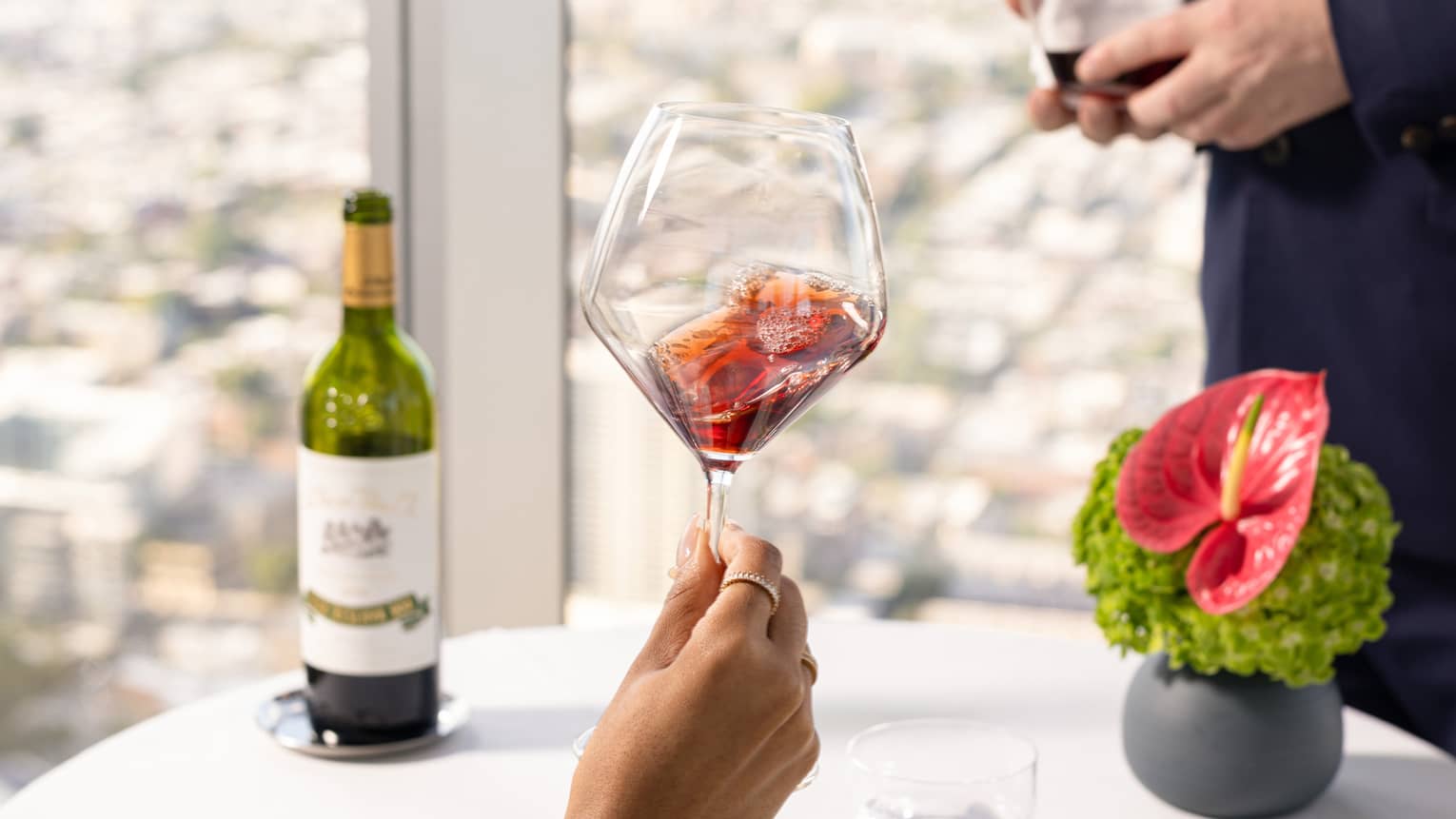 Waiter serving a woman wine who is seated at a white table with a view of the city