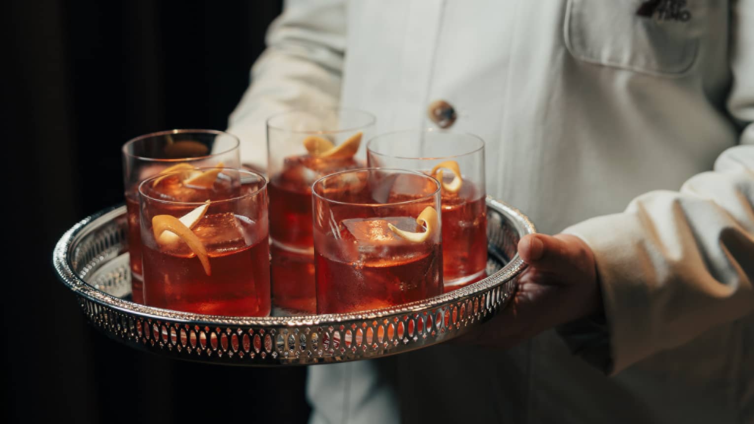 Bartender carries a silver tray of Old Fashioned cocktails