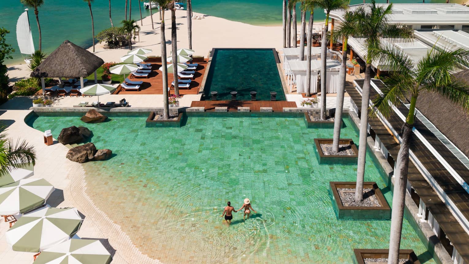 Aerial view of a resort pool adjacent to white-sand tropical beach