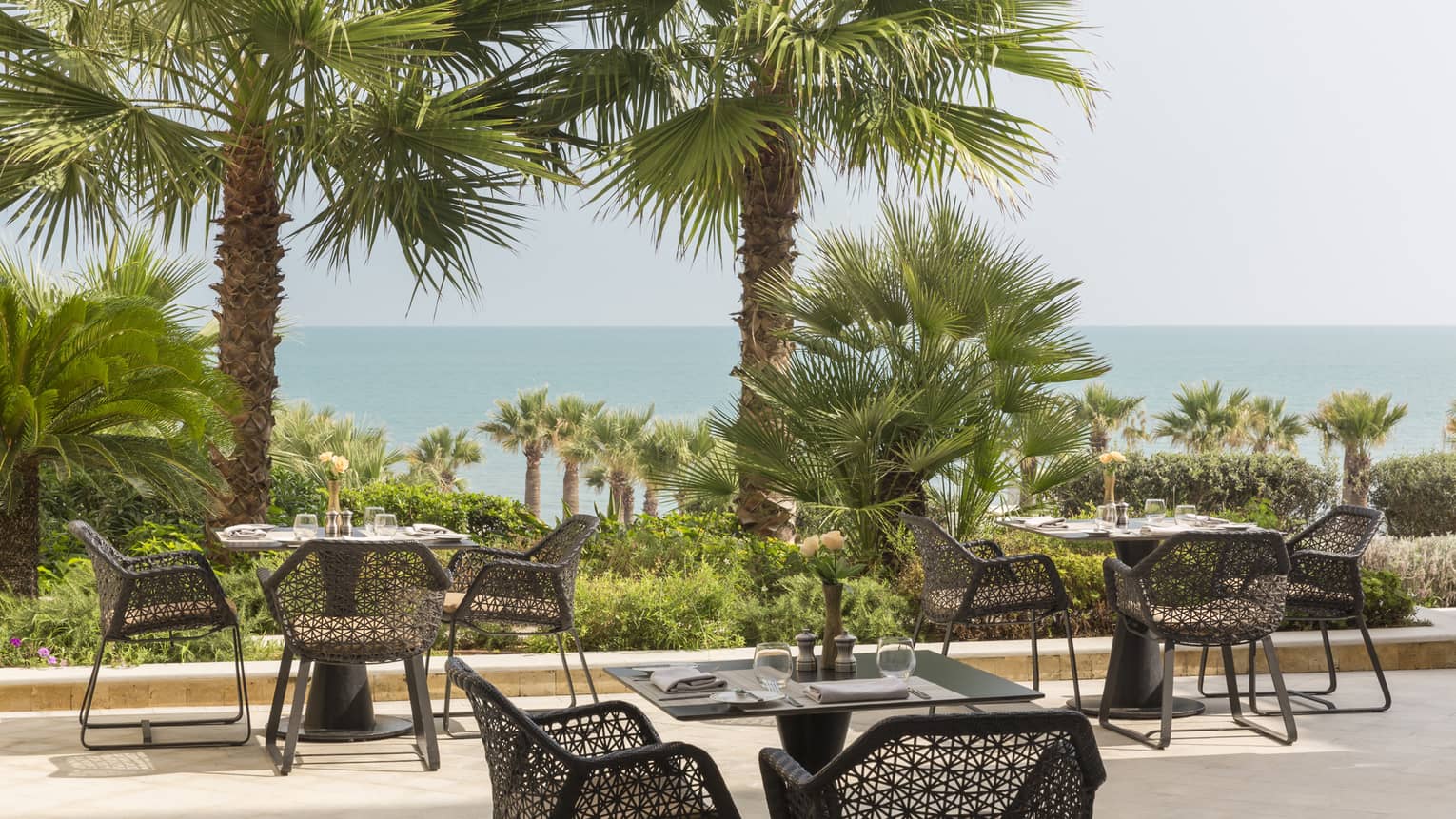 Black tables and geometric black chairs at outdoor bistro overlooking palm trees and ocean 