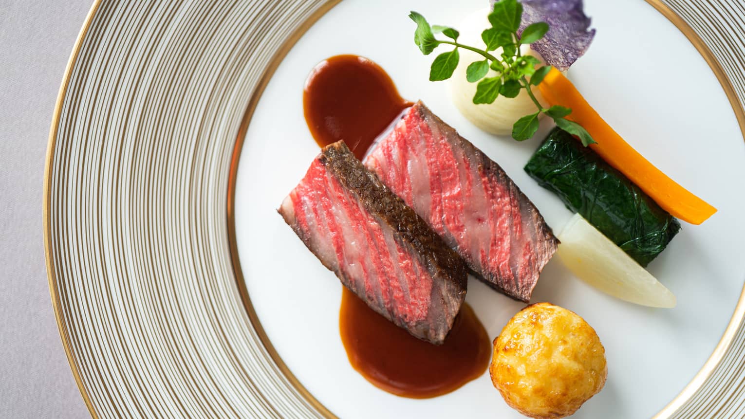 Aerial shot of grilled NY strip steak (rare) with demi-glace and vegetable garnishes