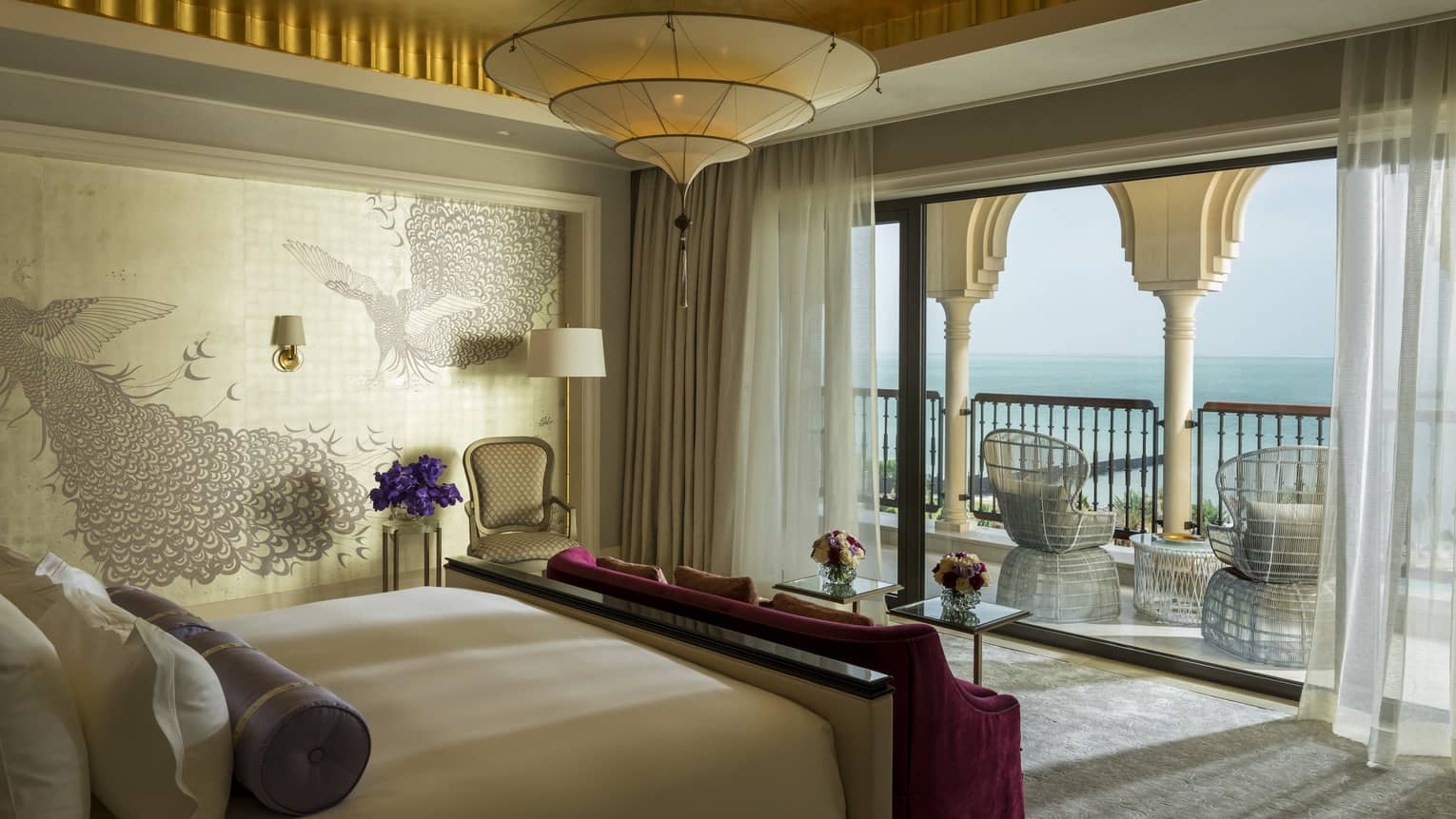 Bedroom suite with decorative wallpaper, red velvet bench, patio with white pillars, wicker chairs