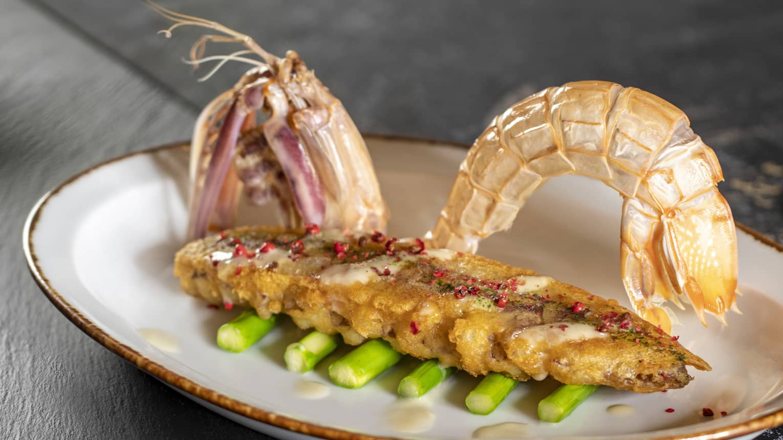 Shell-on prawns on bed of asparagus spears in oval white dish with gold rim