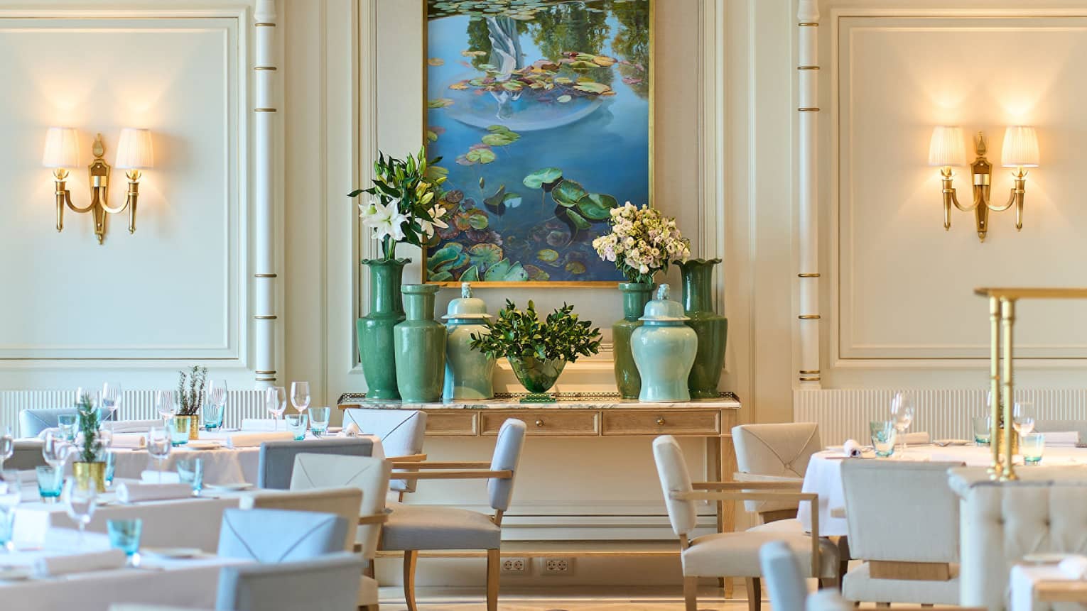 Brightly lit dining room of Riviera with lighted wall sconces, pale blue and white chairs, shiny patterned floor