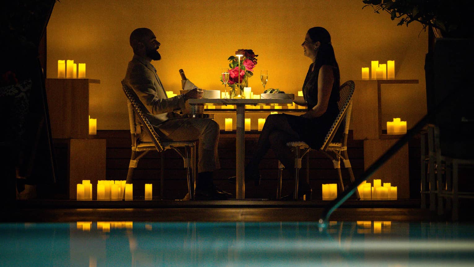 Man and woman sitting at table outdoors, surrounded by candles.