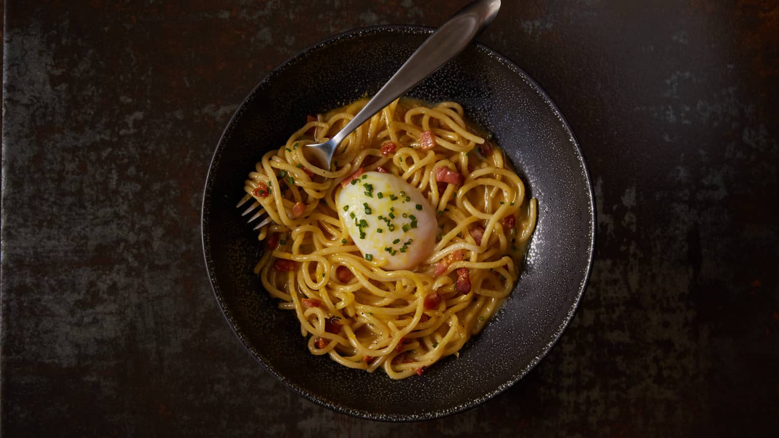 aerial view of black bowl with yellow noodles in sauce, poached