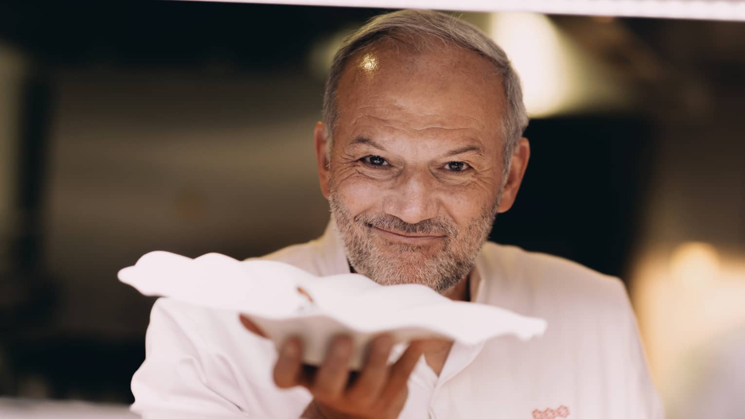 Chef Christian Le Squer smiling, handing out white scalloped dish