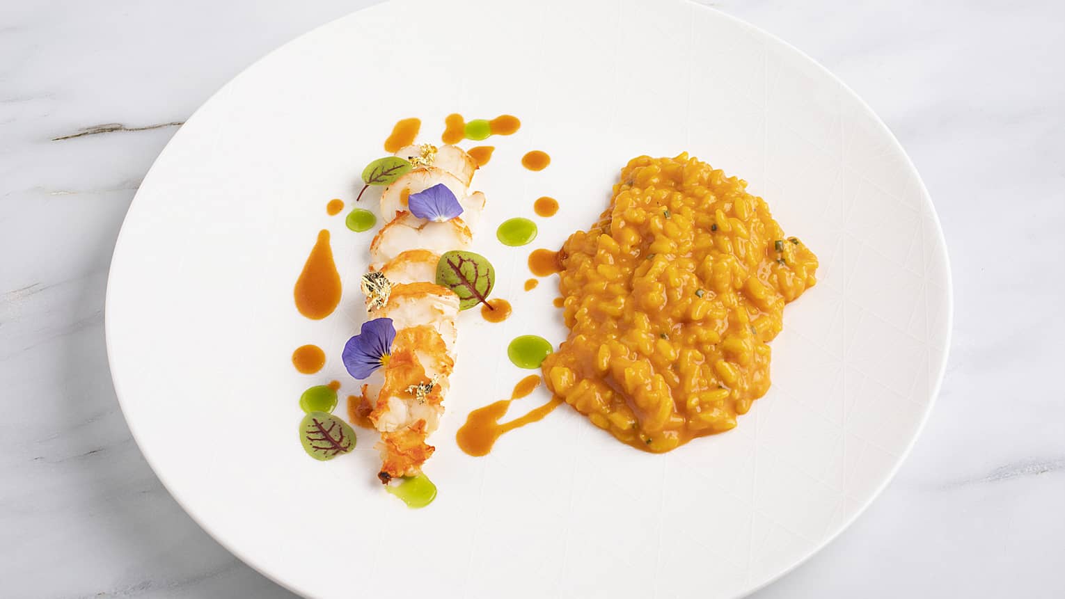 Risotto topped with red and green sauce, and served beside filet-of-fish, all served on a white porcelain plate.