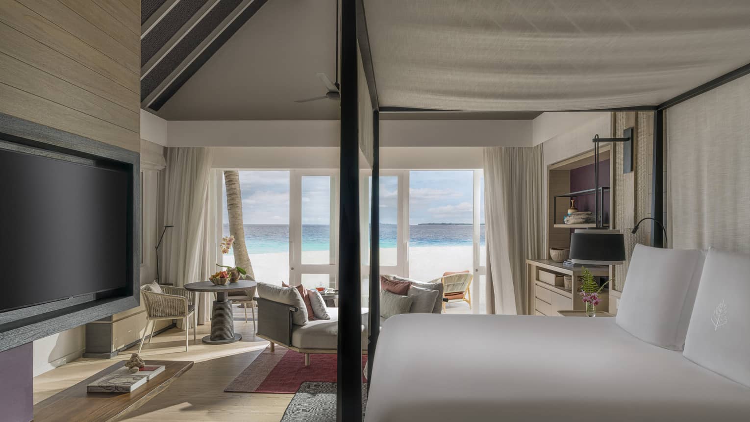 Luxury resort bedroom with four-post king bed, TV, sitting area and walk-out beachfront terrace