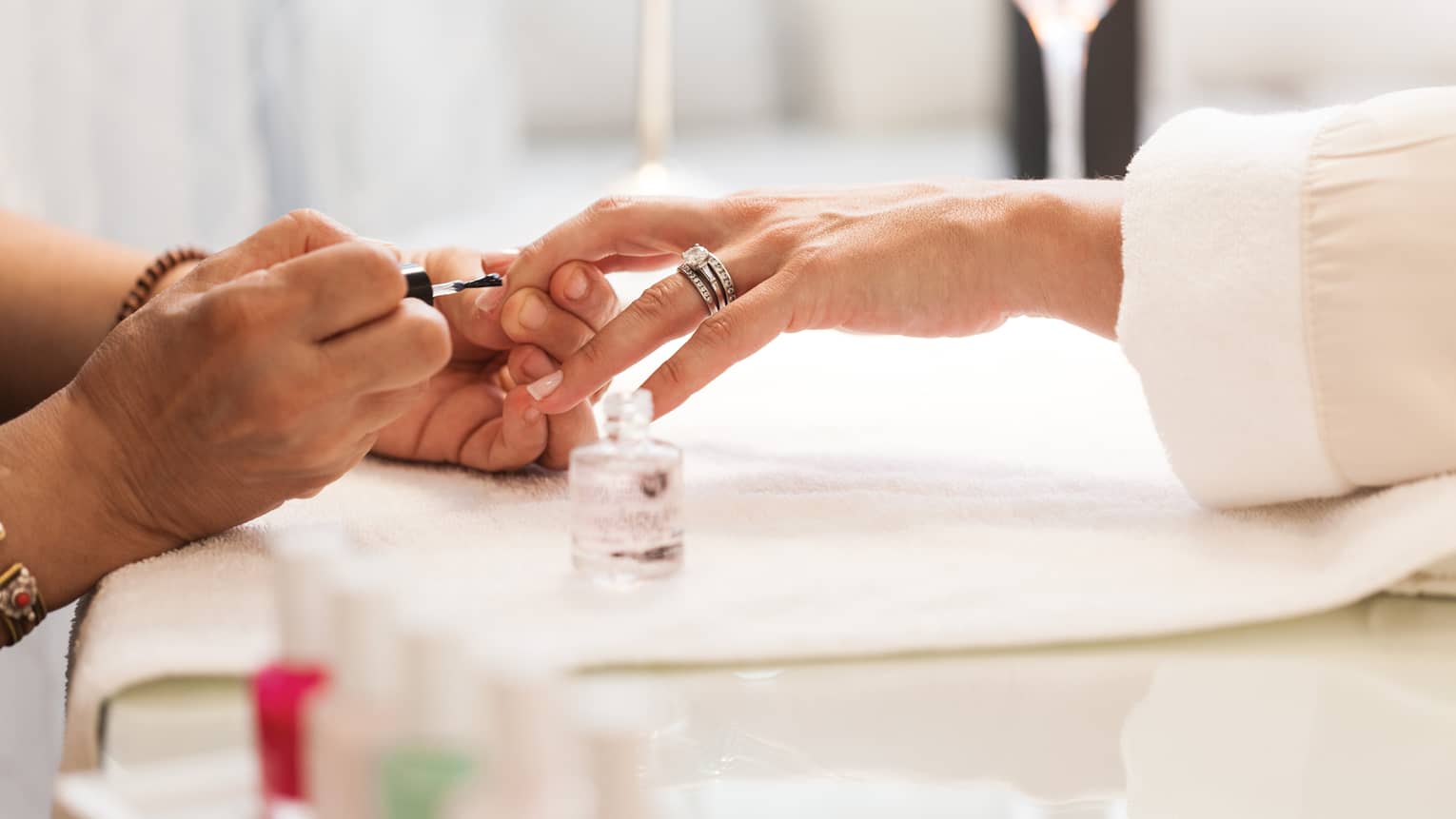 Close-up of woman in white robe getting clear polish manicure at spa table