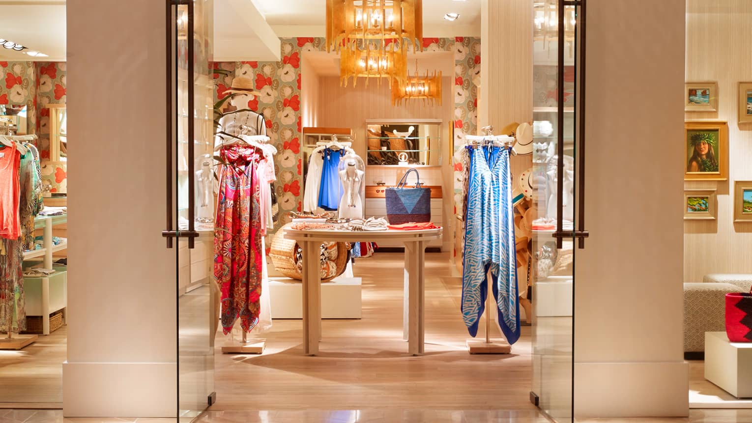 View through doors into boutique lobby store with colourful dresses on racks, table with scarves, purse
