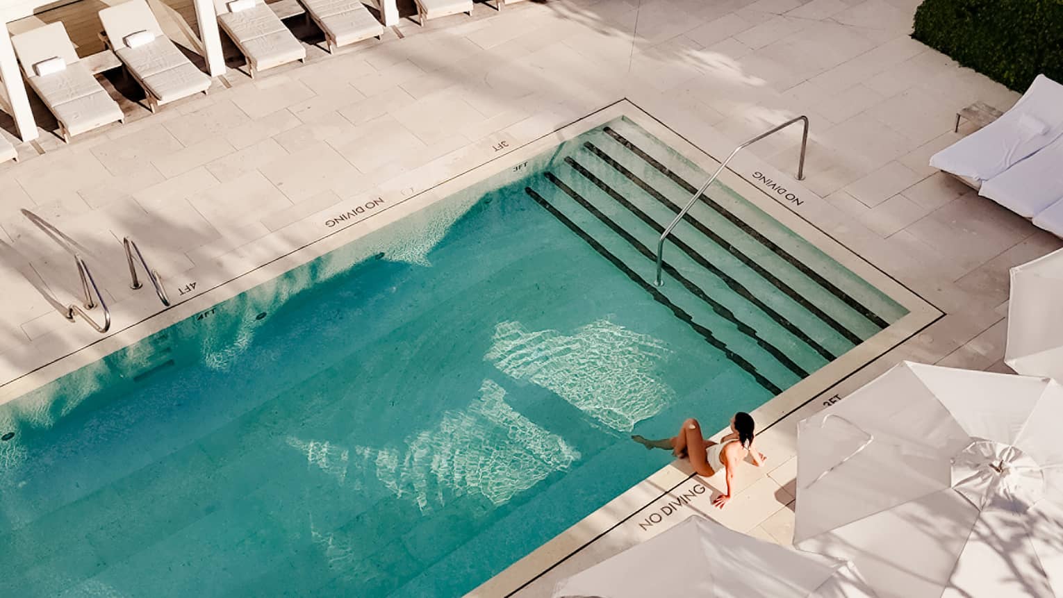 Aerial view of outdoor hotel pool surrounded by white lounge chairs and umbrellas
