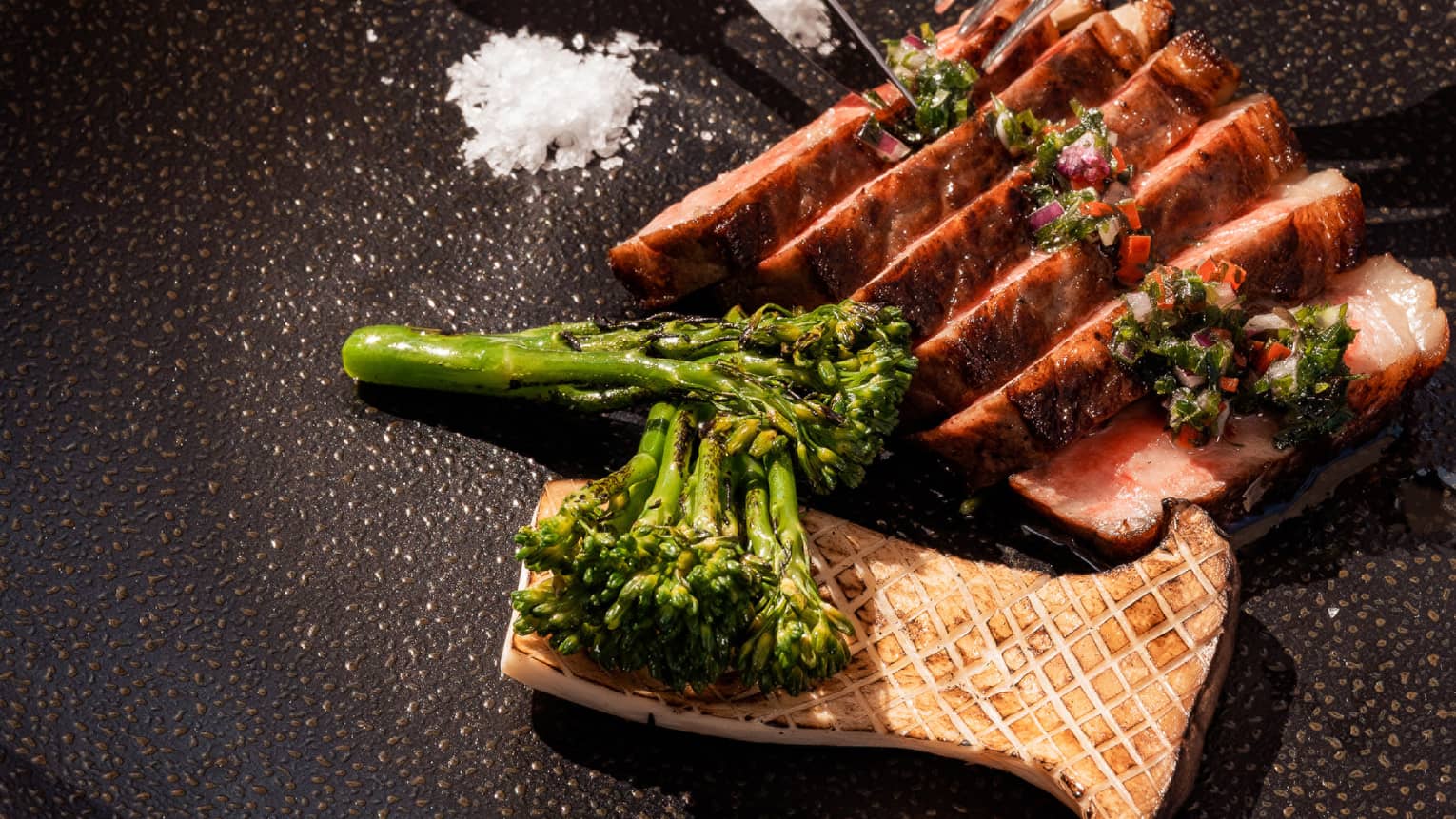 A cut of Wagyu beef tossed with salt and steamed broccoli on a black plate.