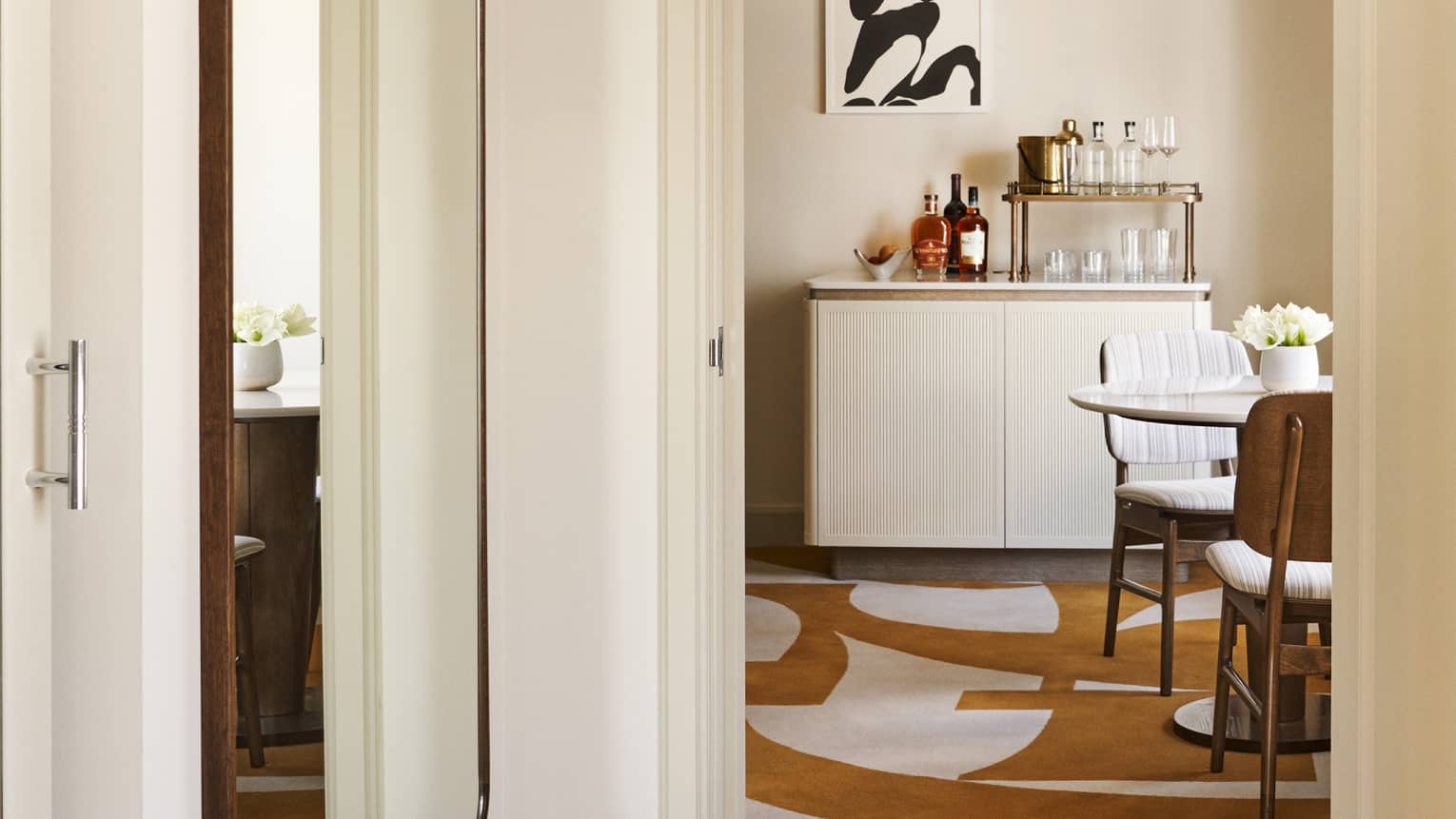 Hotel suite hallway with long mirror on the wall, amber and white abstract carpeting, wet bar and table with two chairs