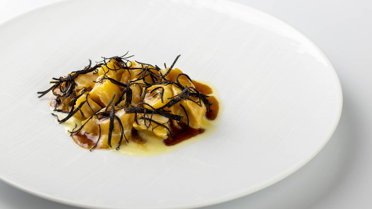 Meat-filled pasta parcels topped with shaved black truffle on round white plate