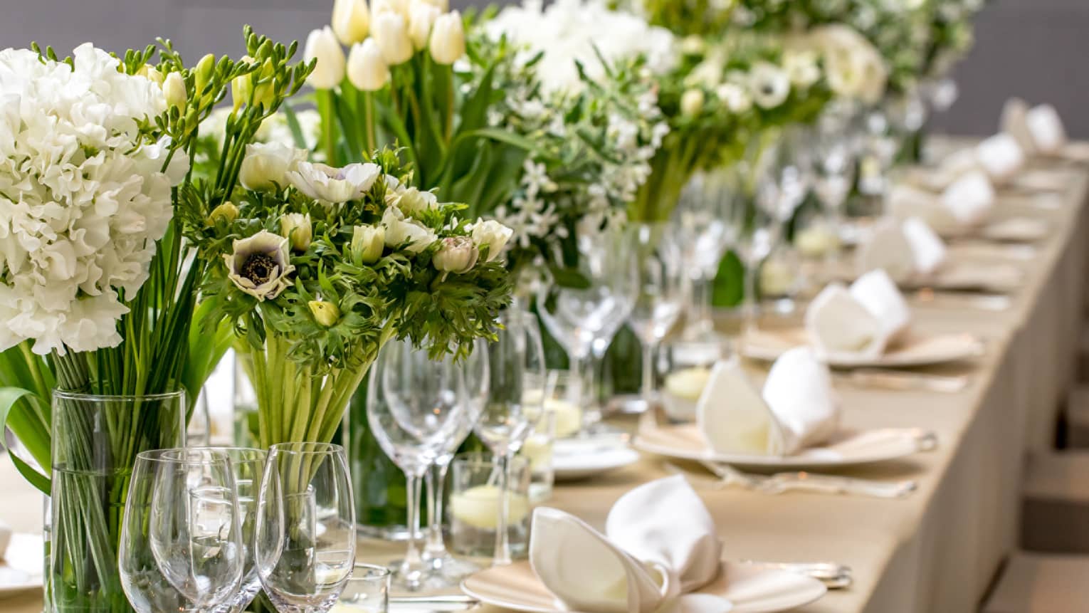 Close-up of long wedding dining table with wine glasses, white flowers in vases 