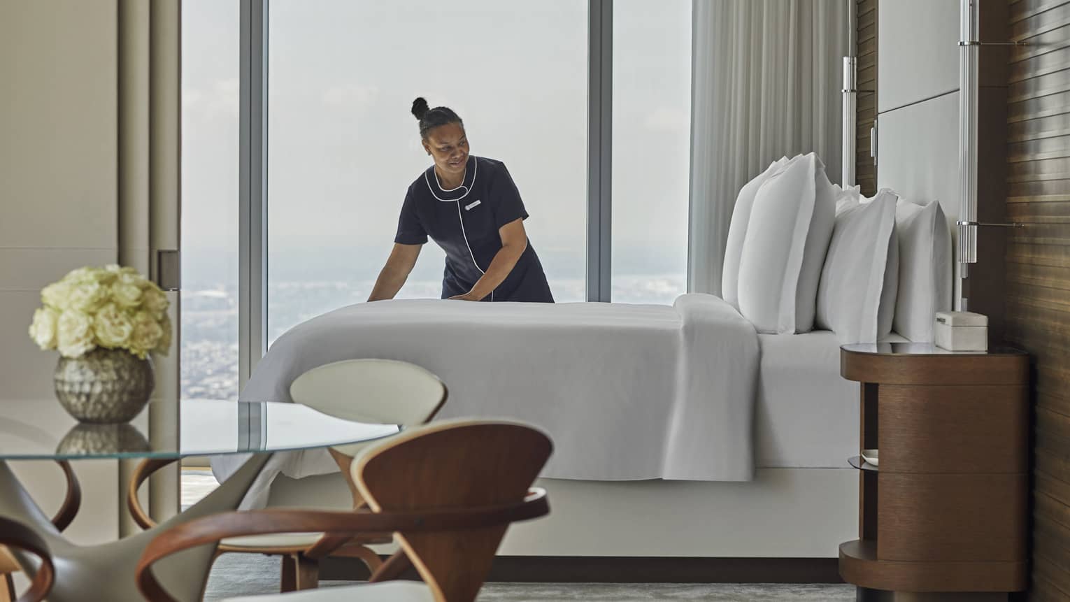 A team member of a hotel making a bed in a hotel room.