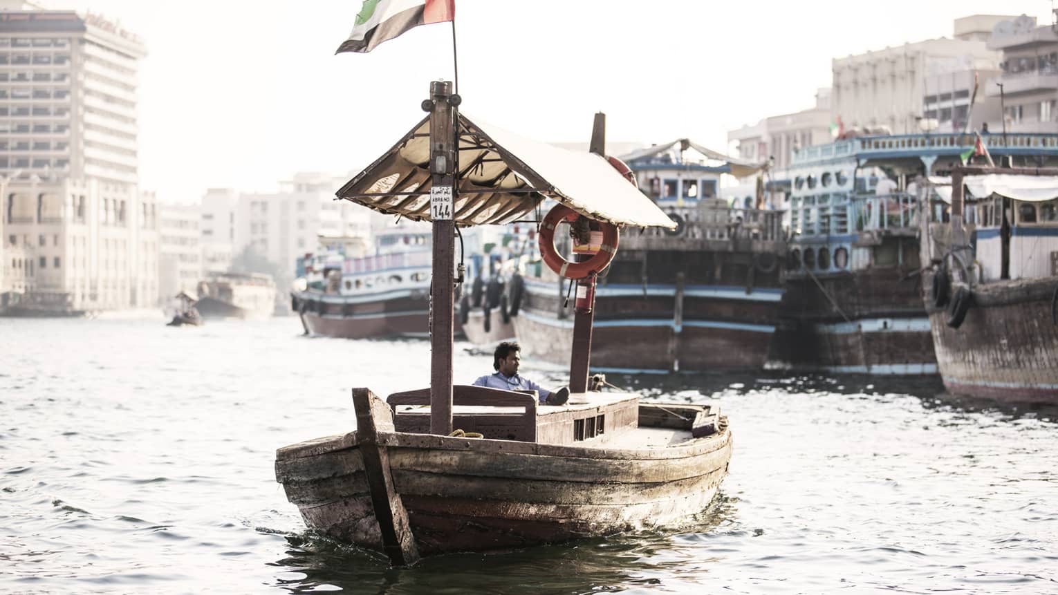 A small wooden boat flying the UAE flag as it sails down a small waterway. 