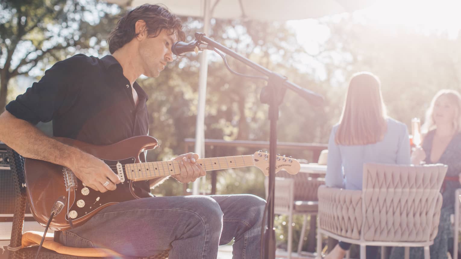 Man plays electric guitar at microphone on sunny patio