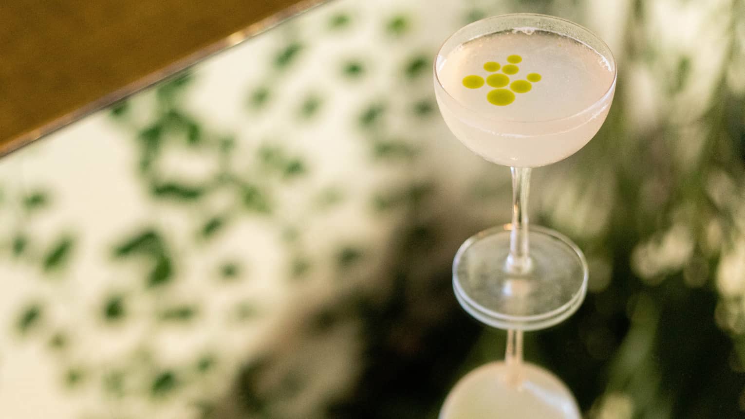 A pale coloured cocktail with green spots of garnish.