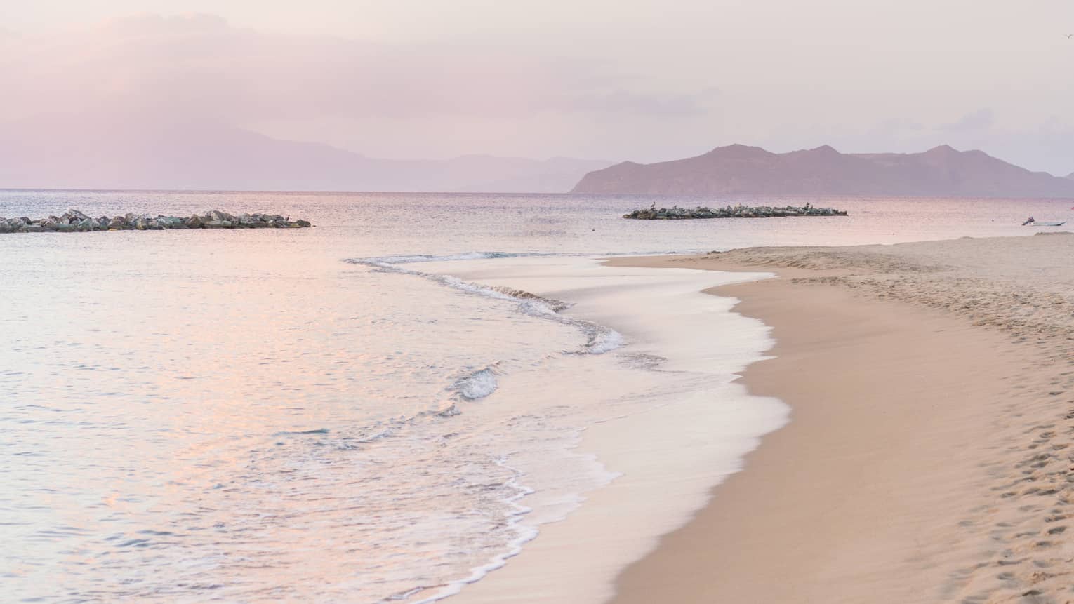 Calm tides on edge of white sand beach, pink sunset reflected on water