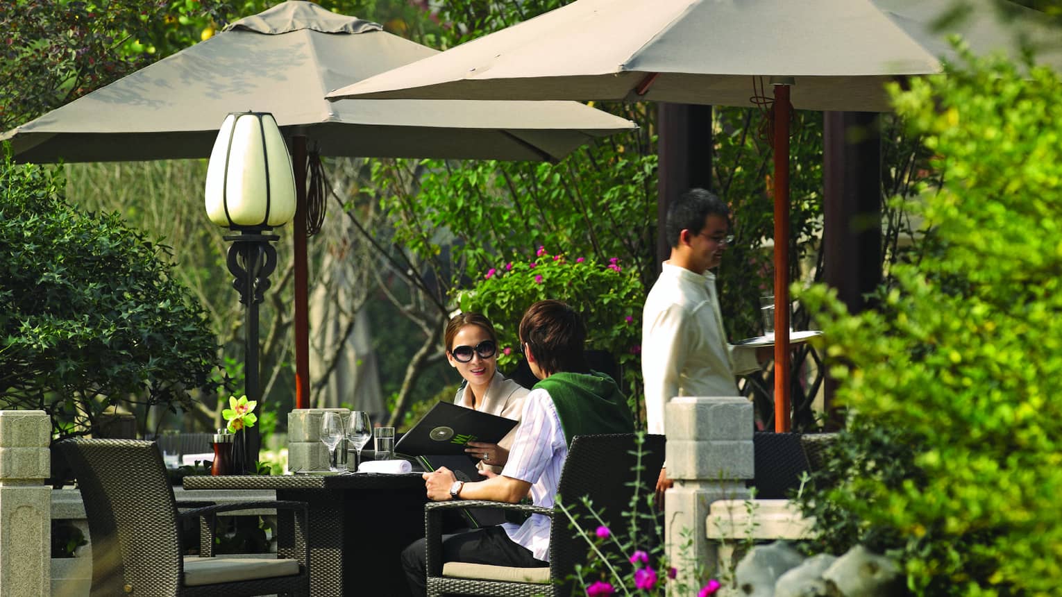 Couple holds menu at patio dining table under umbrellas, pavilion