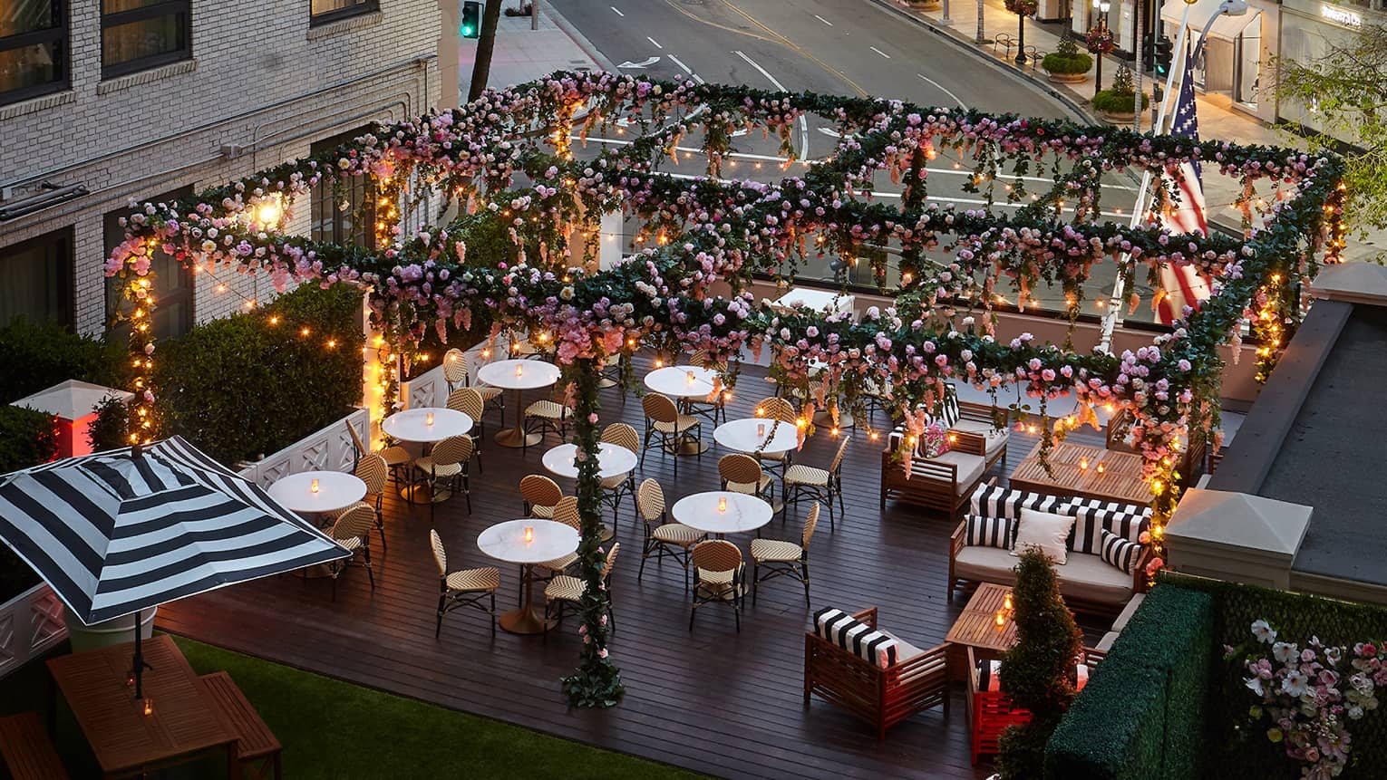 Overlooking Rose Garden terrace with glowing candles on small tables under pergola covered with flowers, vines 