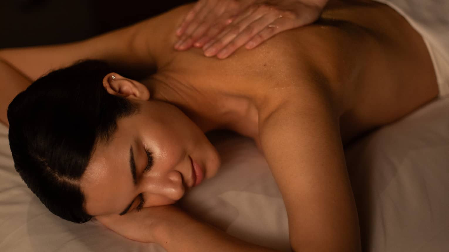 A woman receiving a massage in a dimly lit treatment room.