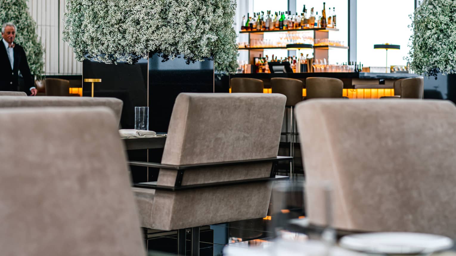 A dining area with beige chairs and place mats, Christmas trees and a bar can be seen on the other side of the room.