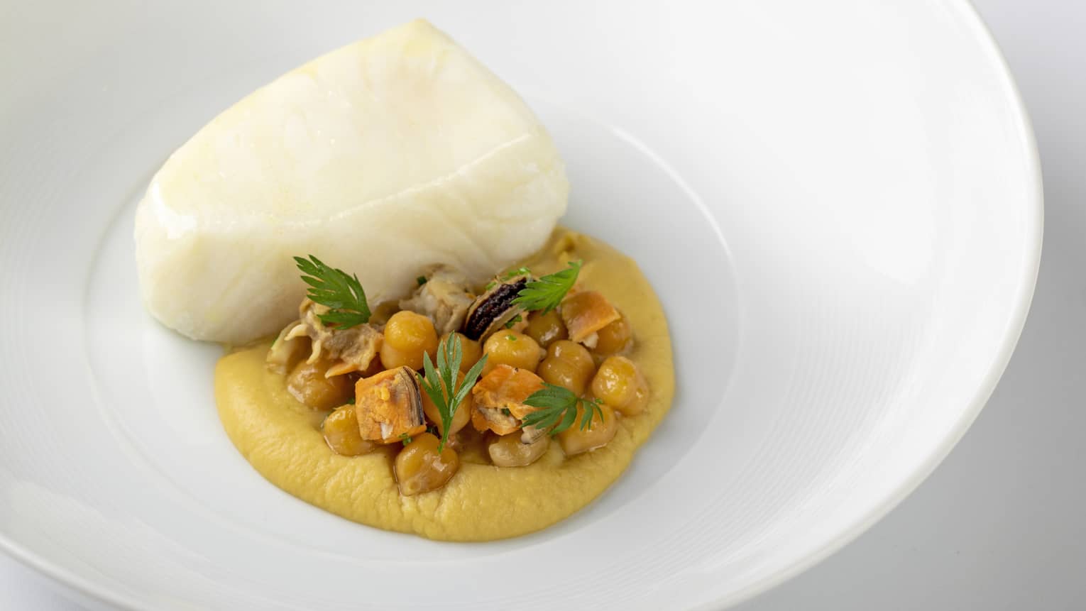 Piece of white fish nestled on bed of yellow sauce with chickpeas and herb garnish