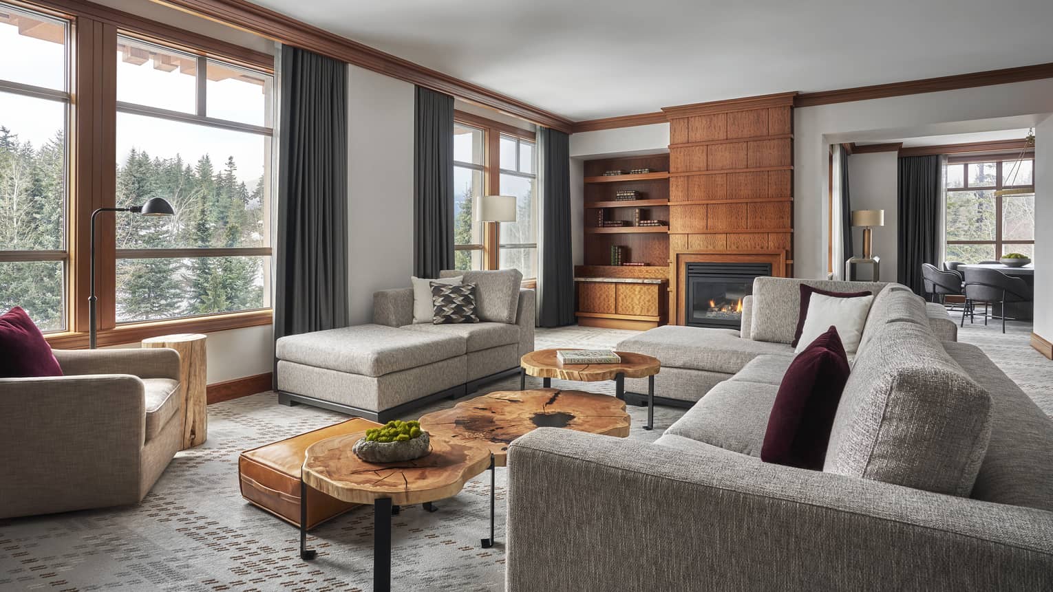 Spacious and stylish Blackcomb Suite at Four Seasons Whistler featuring a sophisticated design with large windows offering a view of the mountains. The suite includes two distinct seating areas: one with a large gray sectional sofa adorned with maroon pillows, and another with a beige daybed by the window. Wooden coffee tables, elegant carpeting, and a built-in wooden shelving unit with a fireplace and a flat-screen TV add to the luxurious feel of the room.,Spacious and stylish Blackcomb Suite at Four Seasons Whistler featuring a sophisticated design with large windows offering a view of the mountains. The suite includes two distinct seating areas: one with a large gray sectional sofa adorned with maroon pillows, and another with a beige daybed by the window. Wooden coffee tables, elegant carpeting, and a built-in wooden shelving unit with a fireplace and a flat-screen TV add to the luxurious feel of the room.