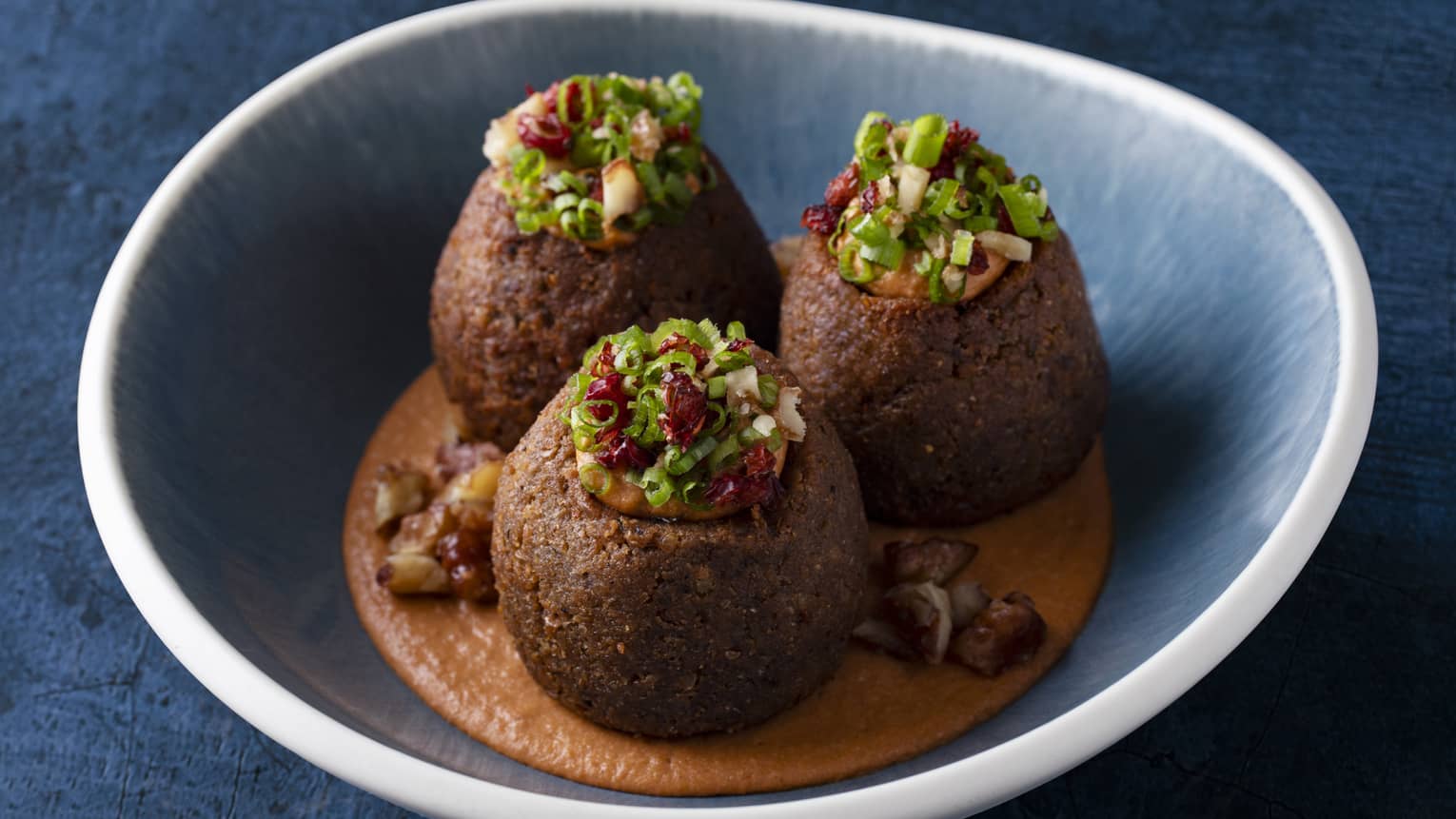  Stuffed meat kebbeh served with a hummus Muhammara dip, and caramelized walnuts in a blue bowl