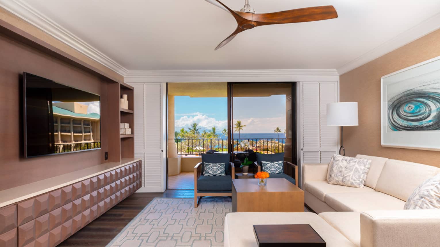 Stylish living room with couch, wooden fan,TV, artwork overlooking ocean and palm trees