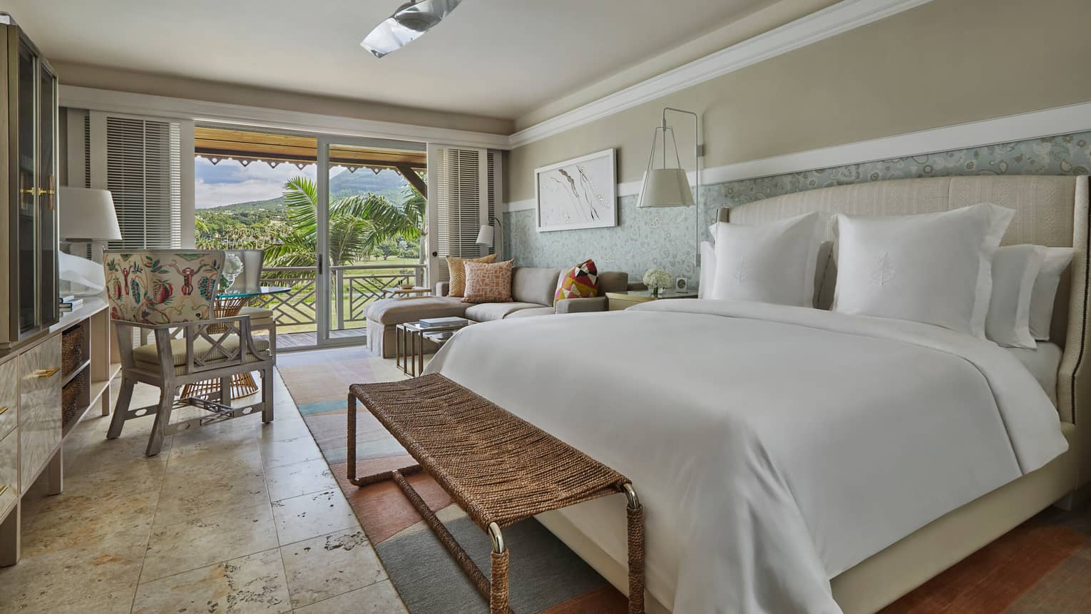 Nevis Peak View Room bed with white linens, wicker bench, sofa and chair, glass patio door