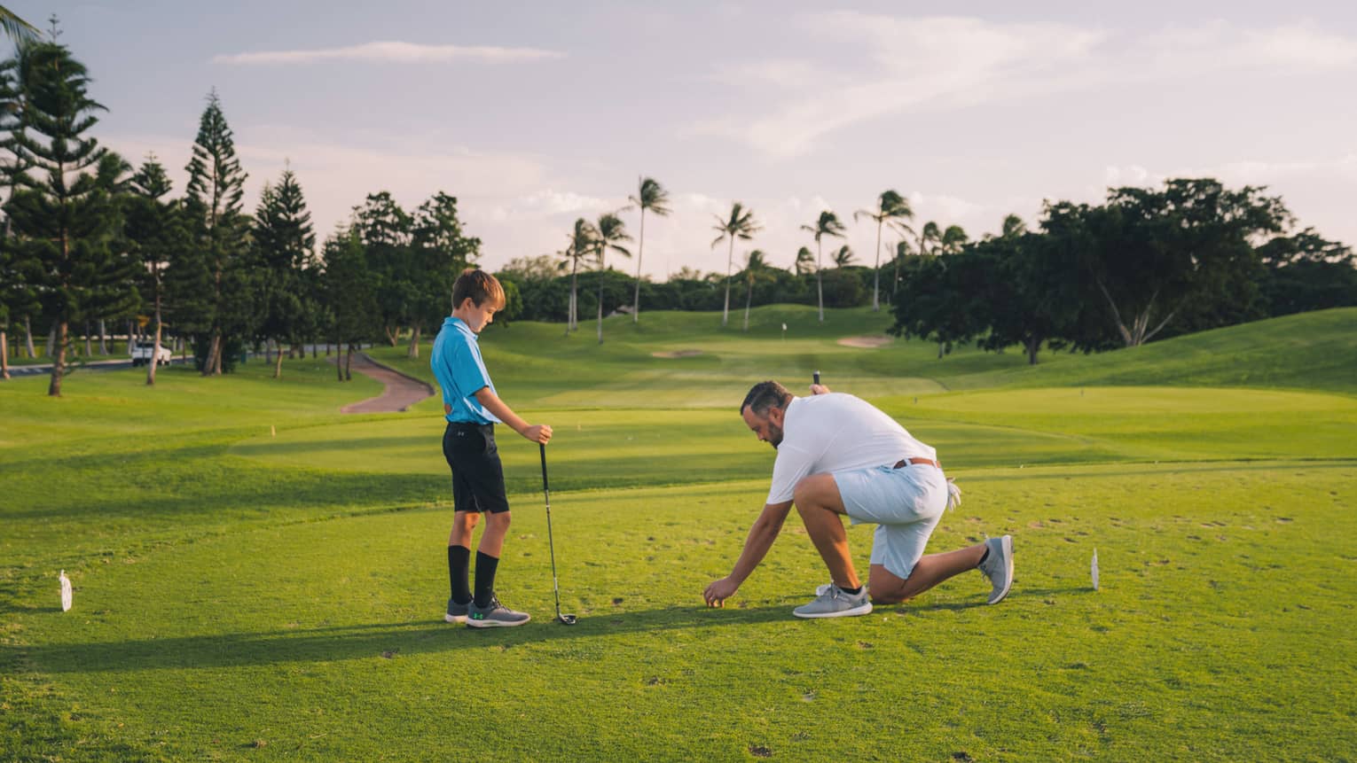 Man and young son play golf on the green, blue sky and palm trees in background 