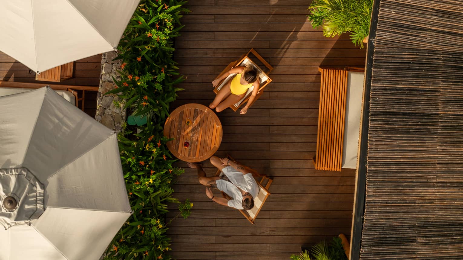 Aerial view of woman in yellow bathing suit and man wearing white shirt and shorts relaxing on lounge chairs on a pool deck