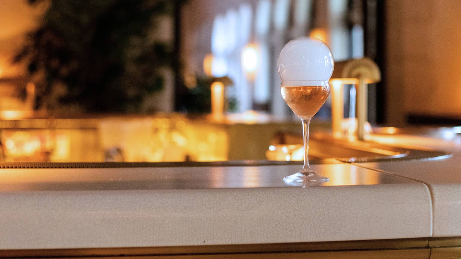An amber coloured cocktail resting on a white bar.