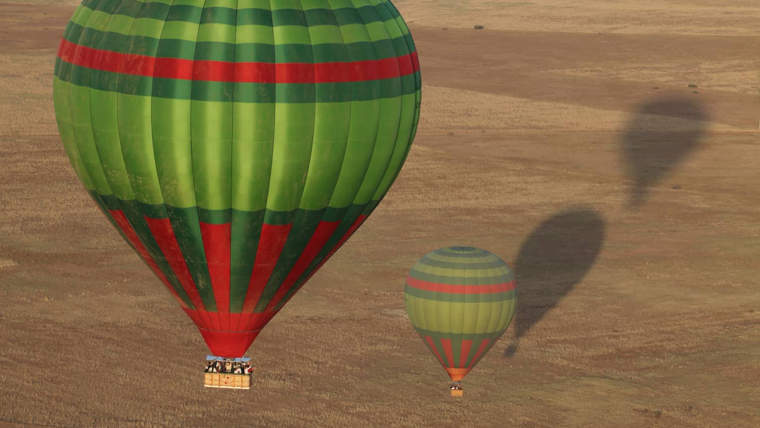Two green and red hot air balloons flying over desert