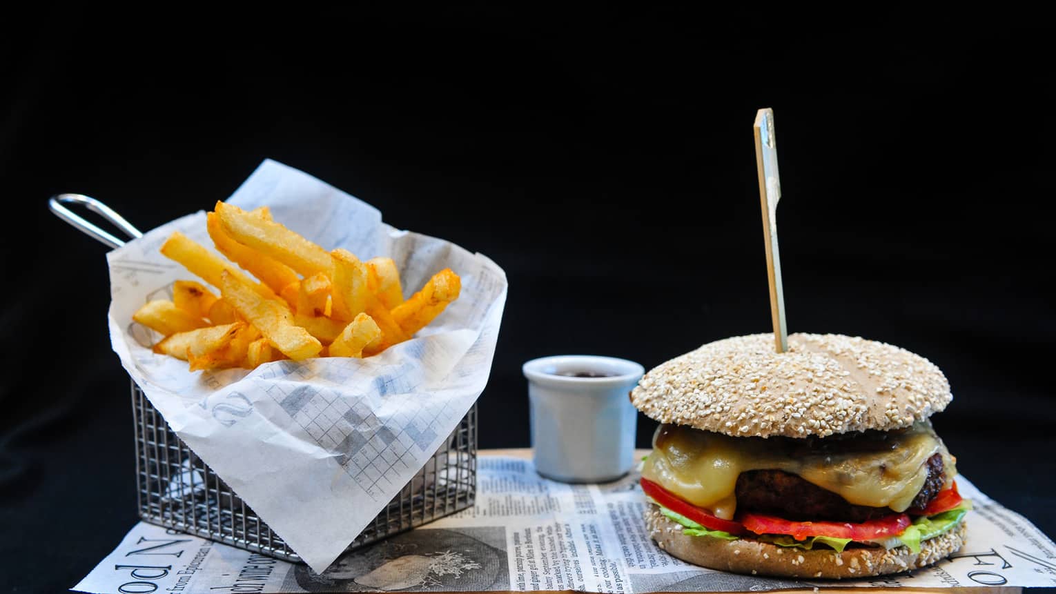 A burger with lettuce, tomato and cheese sits on a tray next to a basket of french fries
