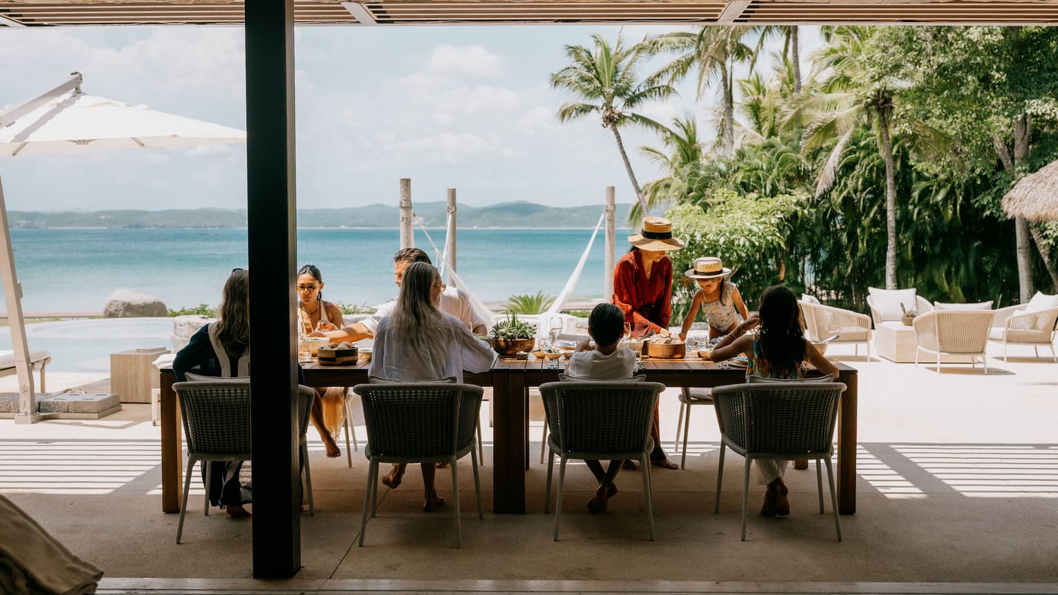 A group of people enjoy a meal in an outdoor dining setting looking out over the beach and ocean.