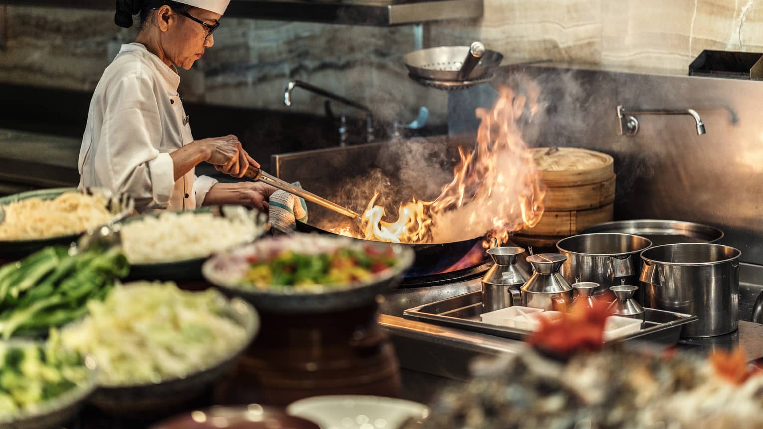A four seasons chef sautees something with a large flame in the kitchen 