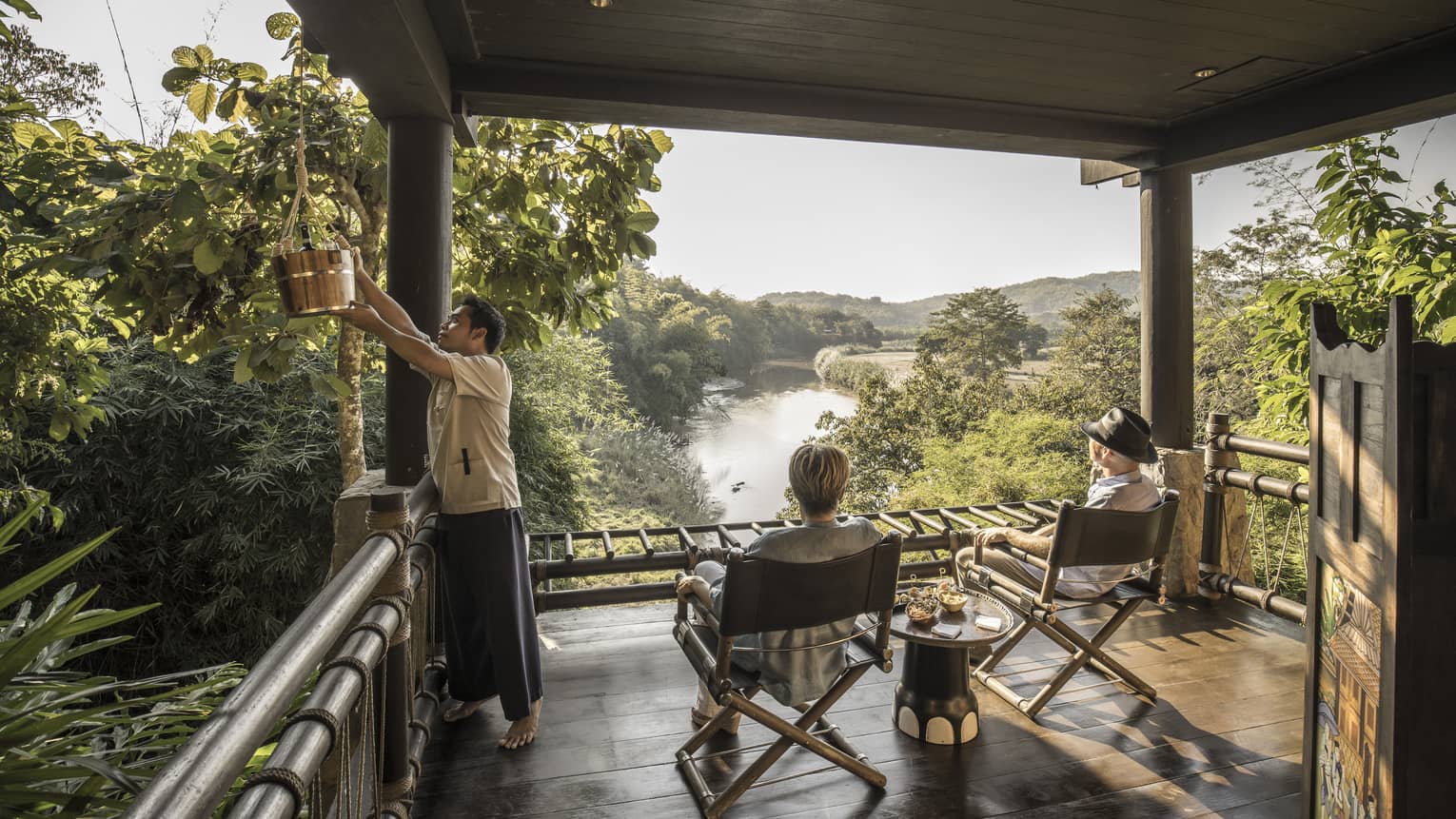 Couple, hotel staff on wood platform patio overlooking the lush Ruak River basin