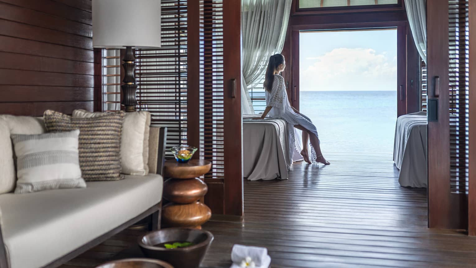 Person sitting on a massage bed in a serene spa treatment room with ocean view, surrounded by cozy seating and wooden décor