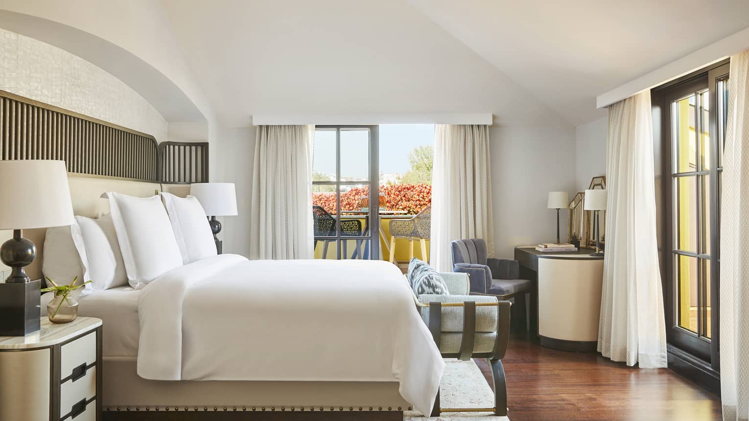White Four Seasons bed flanked by nightstands and lamps, and tall windows with long white curtains on two walls