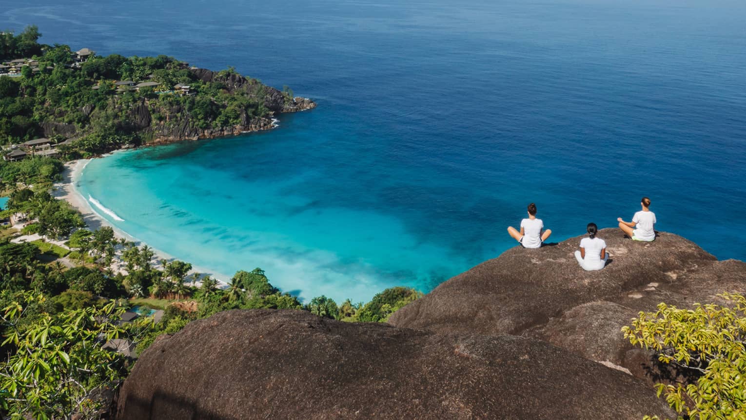 Three people sit cross-legged in meditation overlooking the ocean.